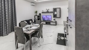 A modern dining area with a marble floor, a dining table set for four, and a television mounted on the wall. - Amour (Rosolini)