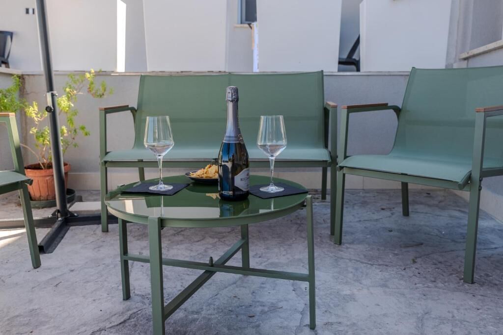 A table with two chairs, a bottle, and two glasses on a glass table.