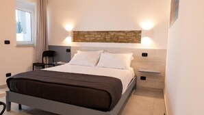 Une chambre moderne avec un lit, des tables de chevet, une fenêtre avec des rideaux et un mur d’accent en pierre.