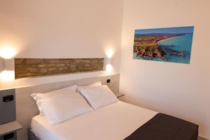 A hotel room with a bed, a stone accent wall, and a coastal view.