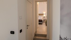 Un couloir étroit mène à une chambre à coucher qui contient un lit et une table de chevet.