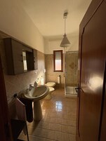 Casa de banho com lavatório, duas sanitas, espelho e chuveiro.