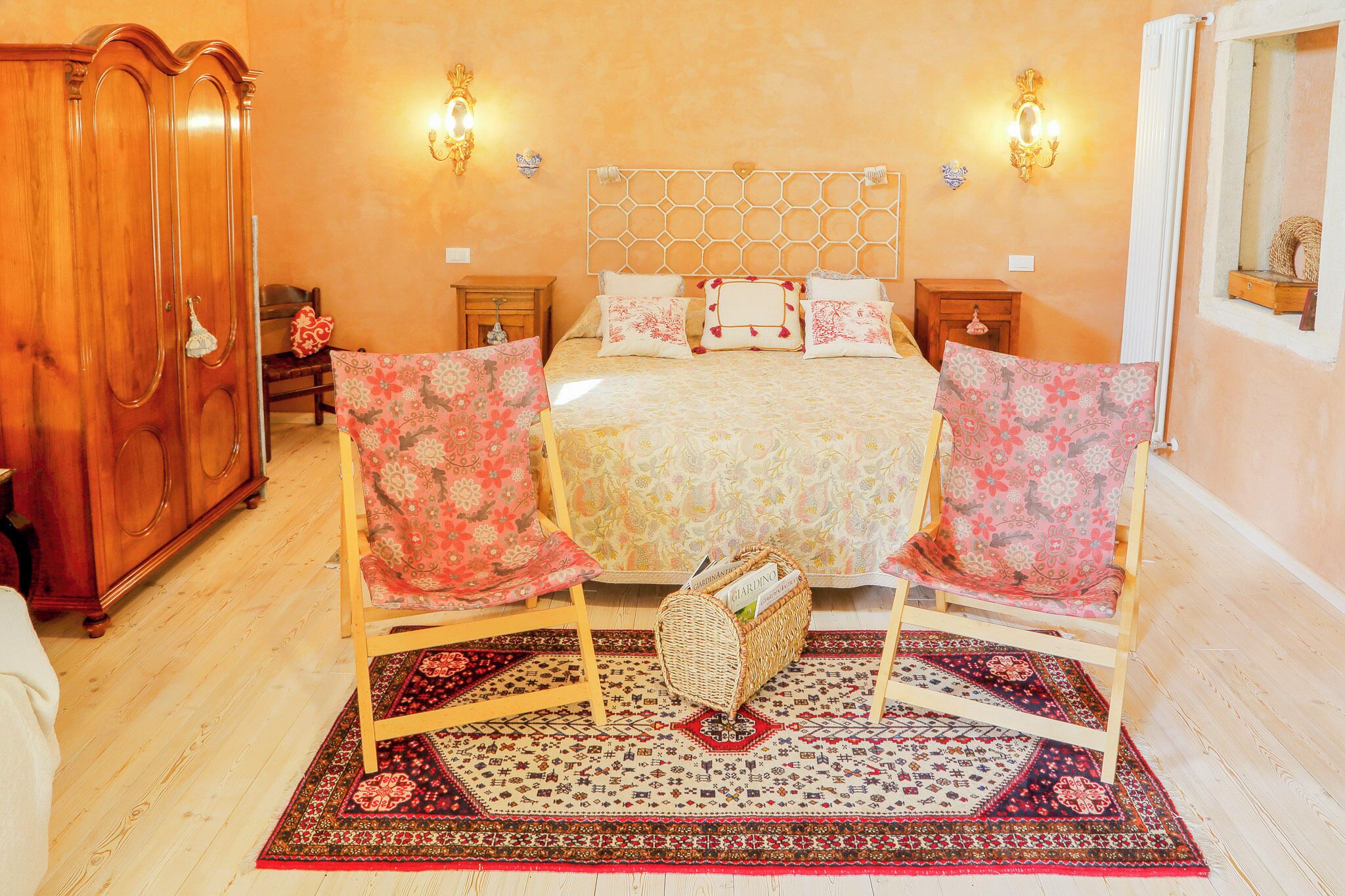 A bedroom with a large bed, two nightstands, a wooden wardrobe, and a patterned rug.