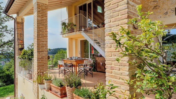 A two-story house with a balcony, outdoor furniture, and potted plants. - Casa in Bioedilizia con Bio Piscina Naturale – Ai Due Gelsi (Val Liona)