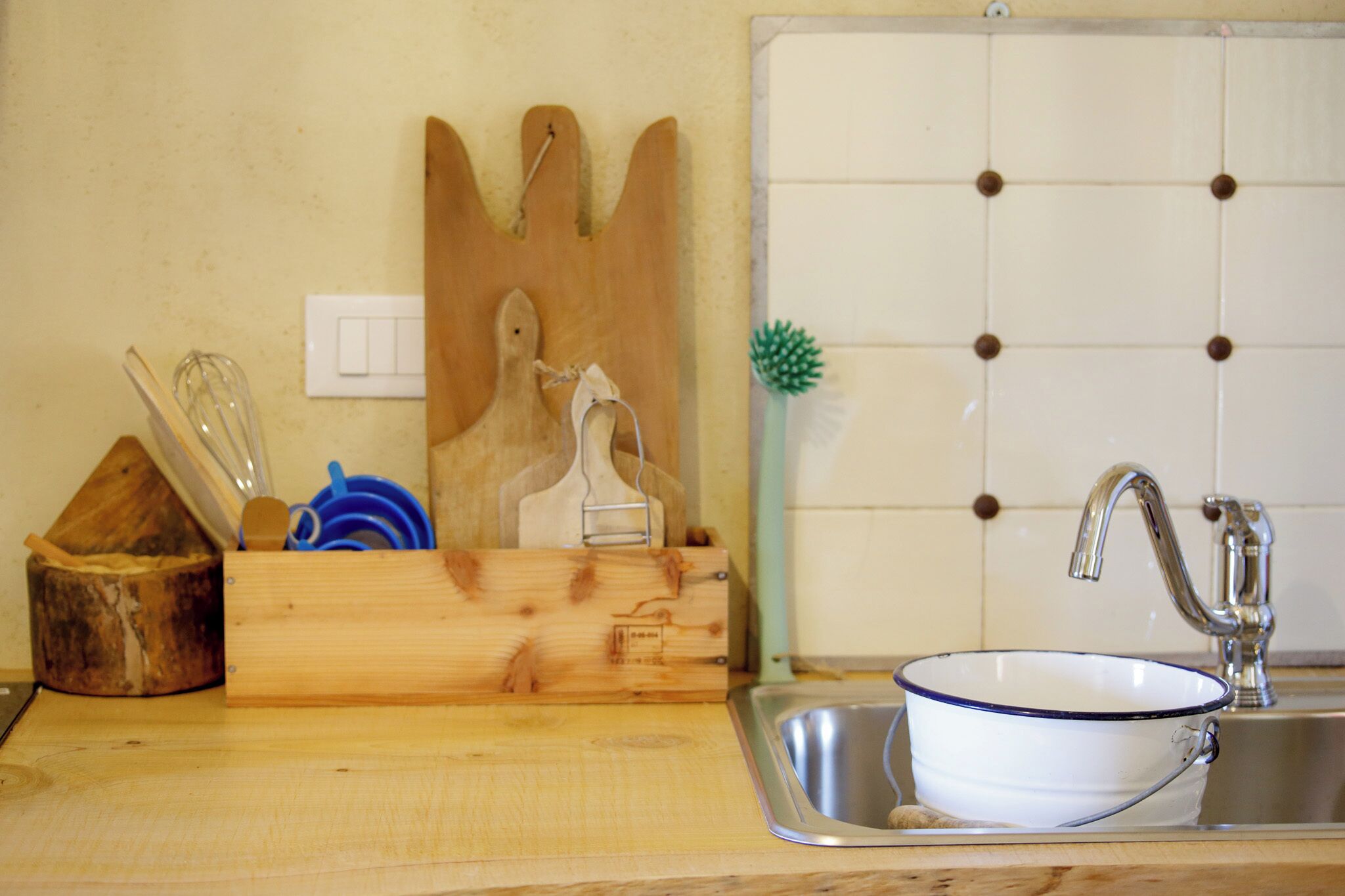 A kitchen with a wooden cutting board, a metal sink, and a blue dish.