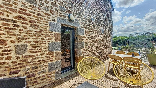 A stone building with a wooden deck, outdoor seating, and a door leading inside.