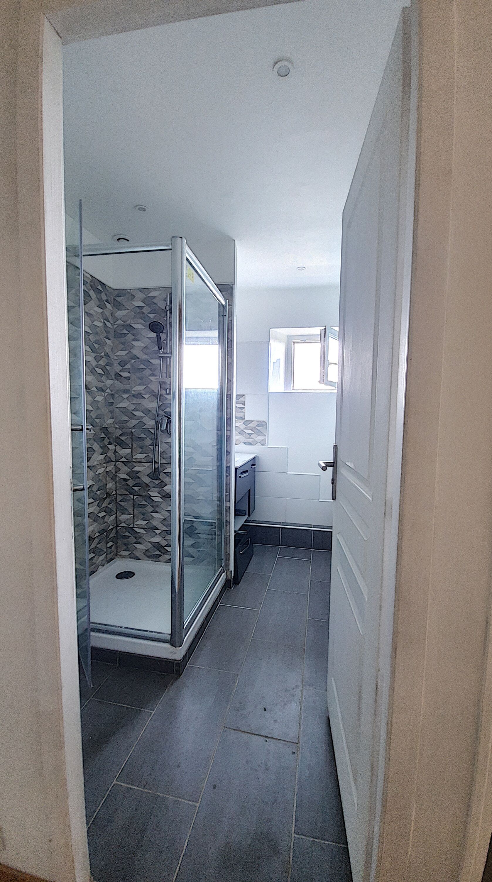 Une salle de bain moderne avec une douche à l’italienne en verre, des murs carrelés et une fenêtre visible.
