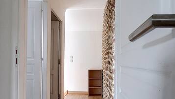 A hallway with wooden flooring, white walls, and a stone wall on one side.