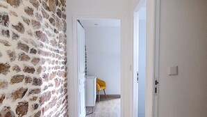 A hallway with a stone wall on one side and a wooden floor. There is a door leading to another room at the end of the hallway.