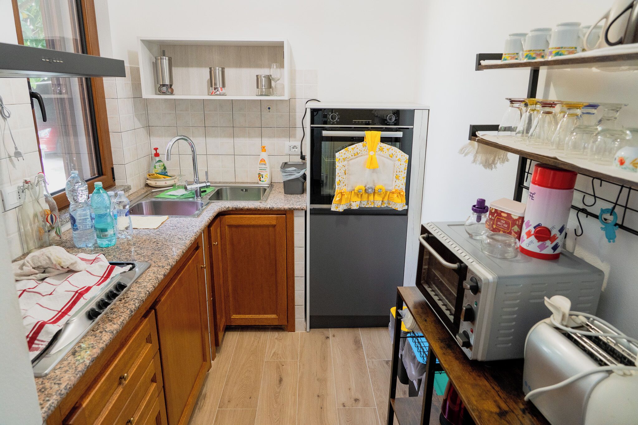 Eine Küche mit Kühlschrank, Backofen, Mikrowelle und Spüle. Es gibt Schränke, eine Arbeitsplatte und ein Regal mit Gläsern.