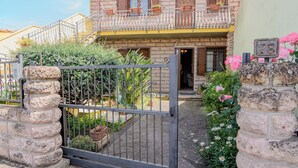 A stone gate with a metal gate, a stone pillar, and a building with a balcony and potted plants.