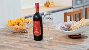 A dining table with a bottle of wine, two glasses, a bowl of oranges, and a bowl of bread.