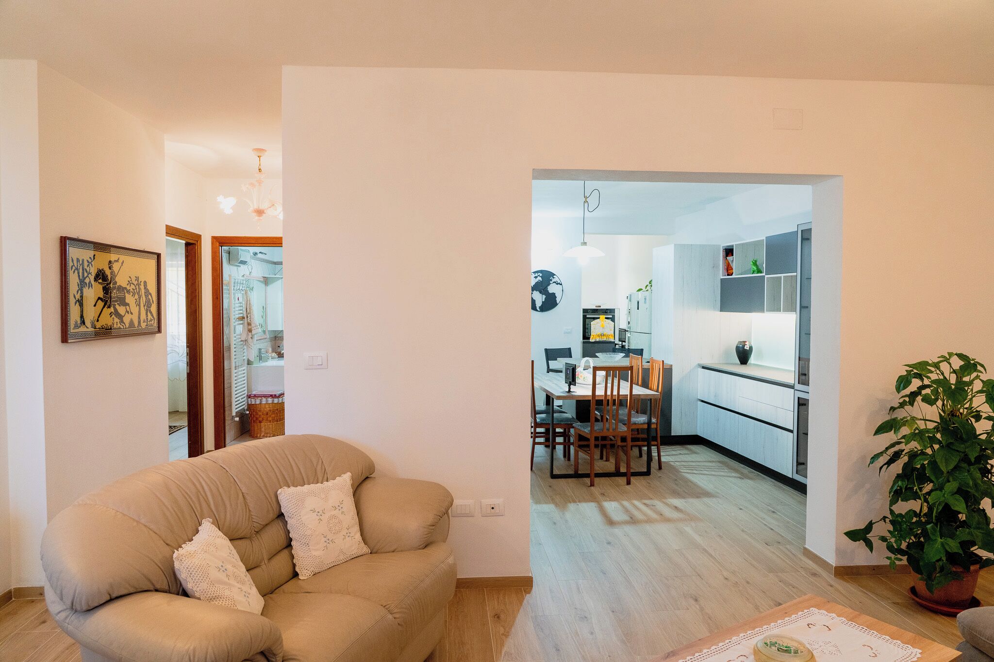 Una sala de estar con un sofá color beige, un comedor con mesa y sillas, y una cocina visible a través de un vano abierto.