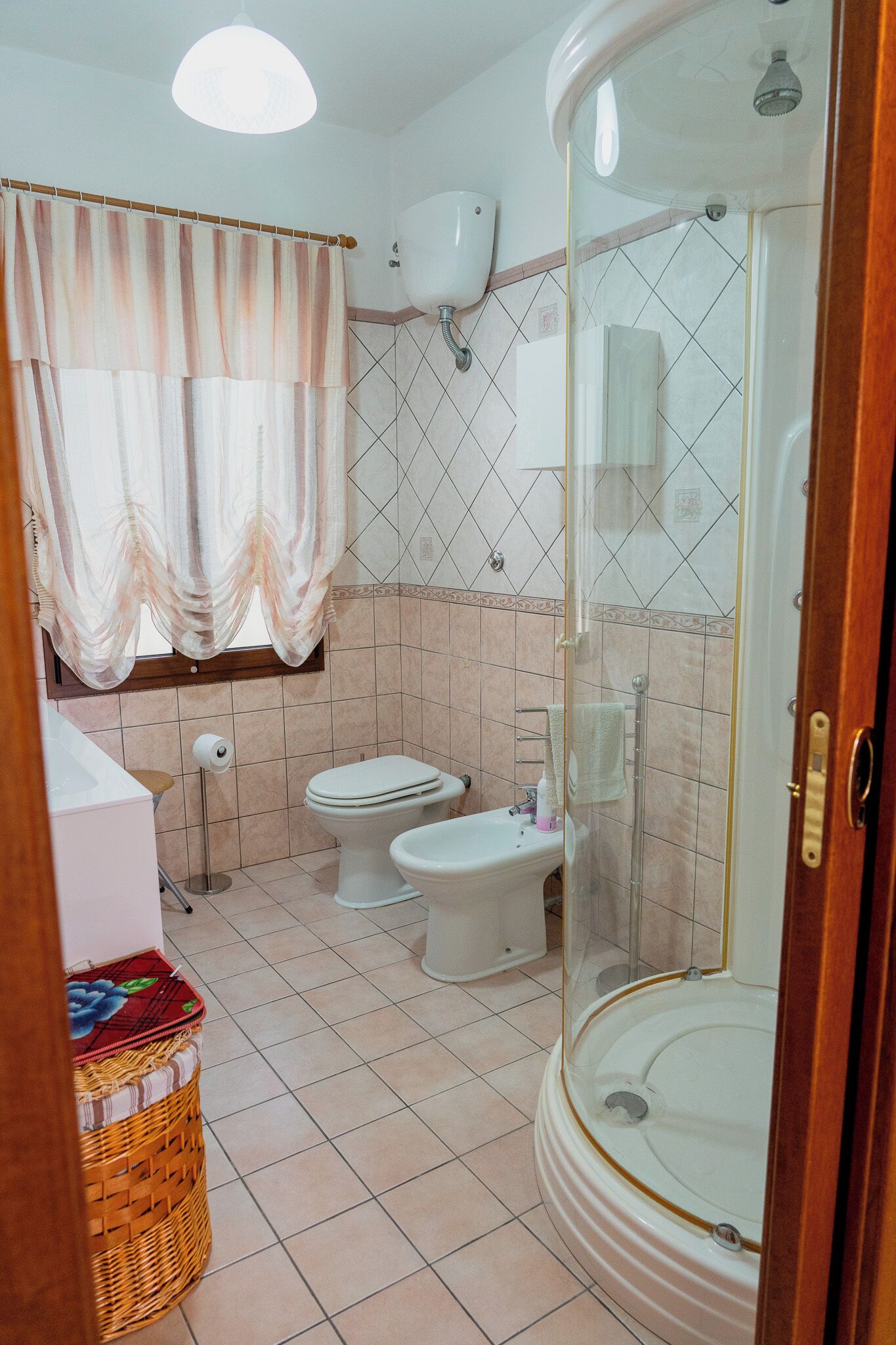 A bathroom with two toilets, a shower, a toilet paper holder, and a basket.