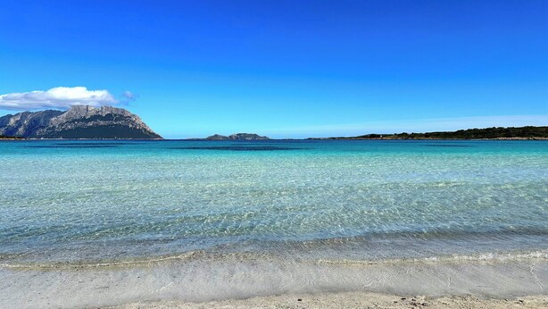 A clear beach with turquoise water, a rocky mountain in the background, and a clear sky. - Casa A.Danieli (Olbia)