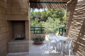 A patio with a stone fireplace, a potted plant, and a white table and chairs. - Casa Onda (Maruggio)