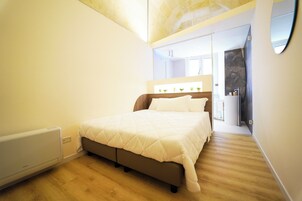 Una camera da letto con un letto, un termosifone, un pavimento in legno e uno specchio a parete.