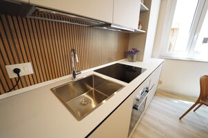 A modern kitchen with a stainless steel sink, wooden panel wall, and a window providing natural light.
