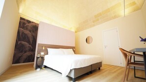 Ein Schlafzimmer mit Bett, Nachttisch, Stuhl, rundem Spiegel und Tür.