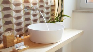 Ein Badezimmer mit weißem Waschbecken, einer Wand mit geometrischem Muster, einer Holzablage und einem Topfpflanzen.