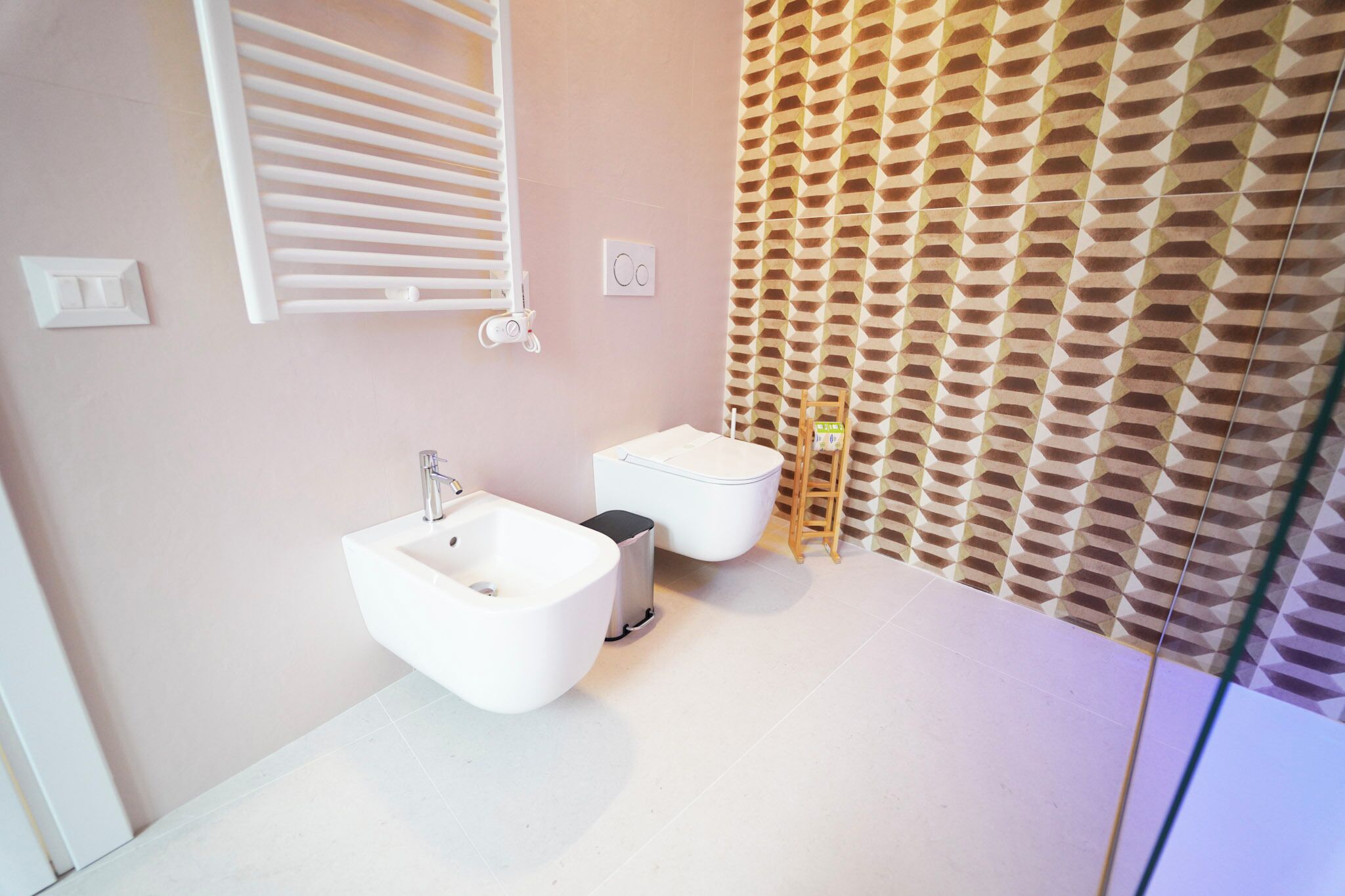 Un baño moderno con bidé, inodoro y pared con diseño.