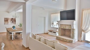 A spacious living room with a fireplace, a television mounted above it, and a dining area with a round table and chairs.