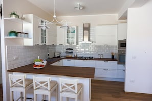 A modern kitchen with white cabinets, a wooden island with bar stools, a stainless steel range hood, and a built-in oven.