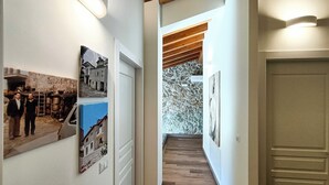 A hallway with wooden flooring, white walls, and a stone accent wall. There are framed pictures on the walls and a door at the end.