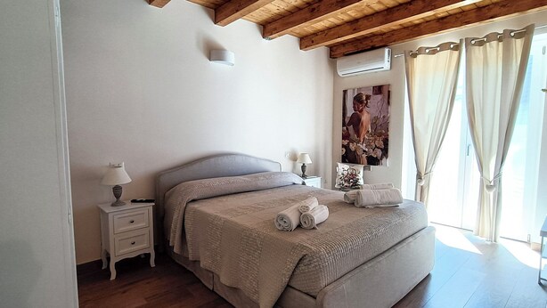 A bedroom with a bed, nightstands, a painting, and a window with curtains.