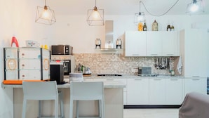 Une cuisine moderne avec des armoires blanches, un îlot central doté de tabourets de bar, un four encastré et des luminaires suspendus.