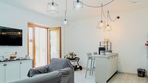 Un salon moderne avec un canapé gris, un coin cuisine doté d’un bar et un téléviseur fixé au mur.