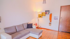 A modern living room with a grey sectional sofa, a floor lamp, and a bookshelf. - San Giacomo Sweet Home (Nettuno)