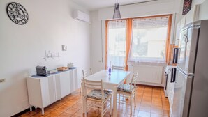 A compact kitchen with a white table and chairs, a refrigerator, and a window with curtains. - San Giacomo Sweet Home (Nettuno)