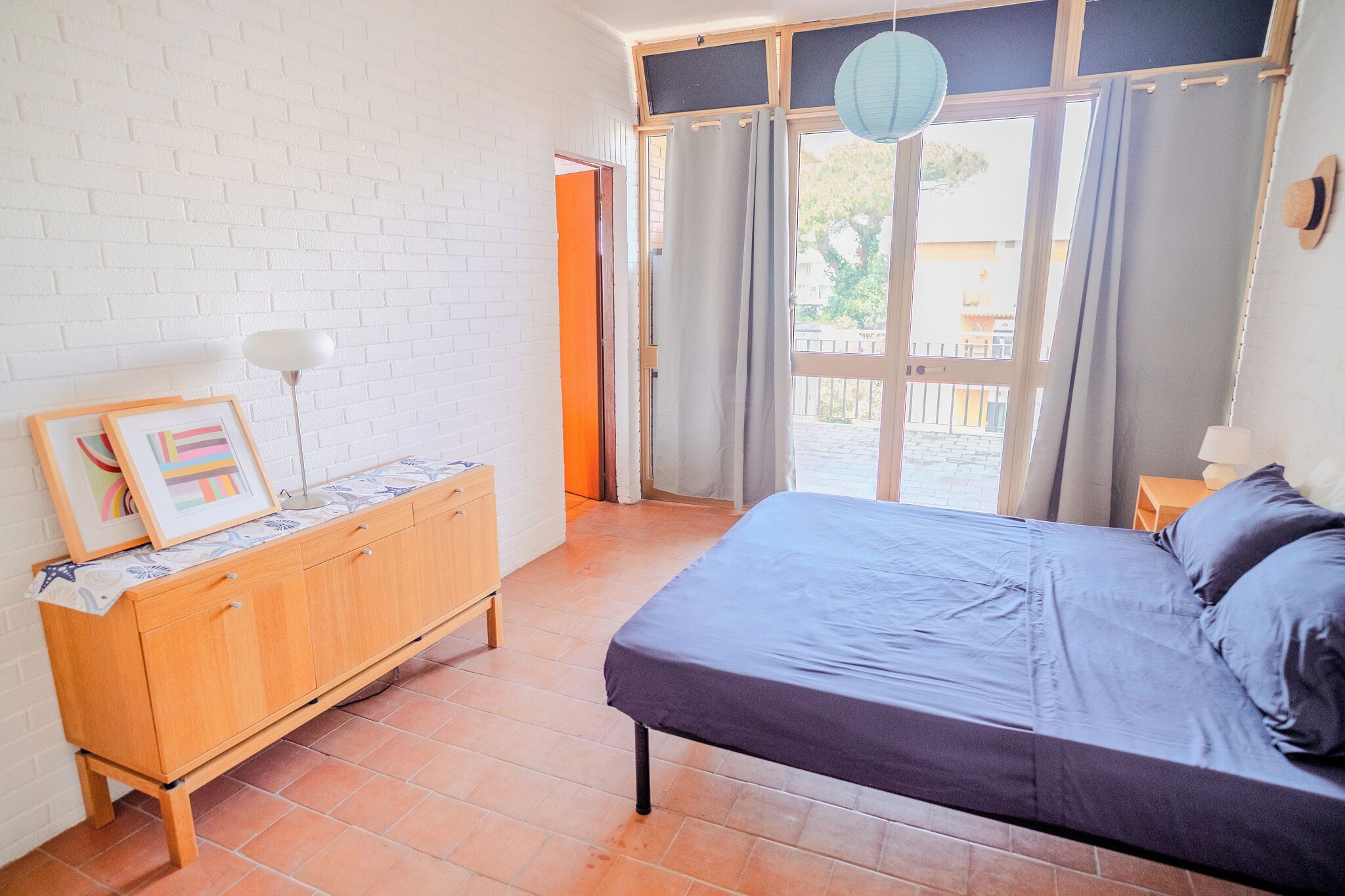 A bedroom with a bed, a wooden dresser, a lamp, and a window with curtains.