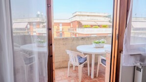 A balcony with a white table and chairs, a potted plant, and a view of neighboring buildings. - San Giacomo Sweet Home (Nettuno)