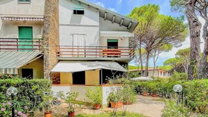 A two-story house with a balcony, surrounded by potted plants and a grassy area with a table and chairs. - La Casina Di Giuliana (Principina a Mare)