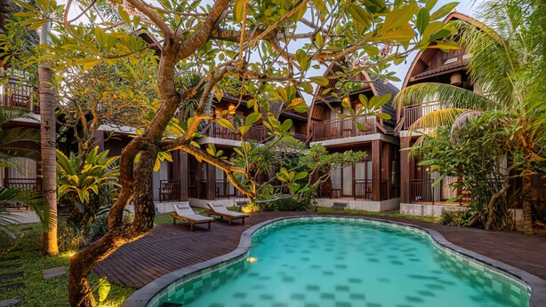 Une piscine entourée d’une terrasse en bois, de palmiers et d’un bâtiment doté de balcons.