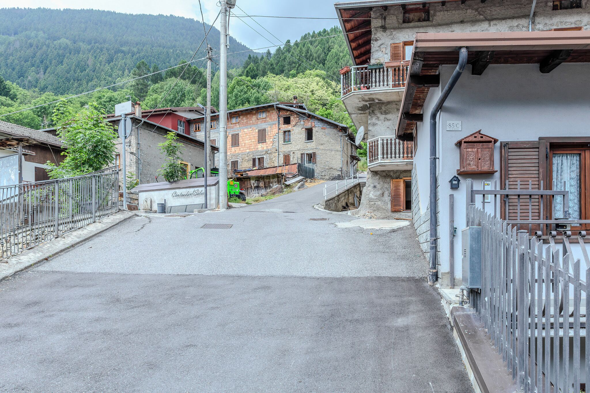 Une rue étroite menant à un immeuble doté d’un balcon et d’une enseigne indiquant une température de 85 °C.