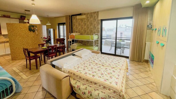 Ein Hotelzimmer mit Bett, Esstisch, Stühlen, einer kleinen Küchenzeile und einem Balkon mit Aussicht.