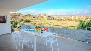 A modern outdoor dining area with a pool table, white chairs, and a scenic view of a rural landscape.