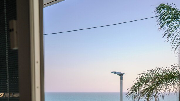A balcony with a view of the sea, a palm tree, and a street lamp. - Casa Vacanze Stella Marina (Marina di Palma)