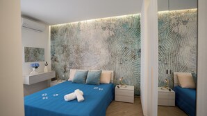 A modern bedroom with a blue bedspread, a bedside table with a lamp, and a wall with a leaf pattern. - Casa Vacanze Stella Marina (Marina di Palma)