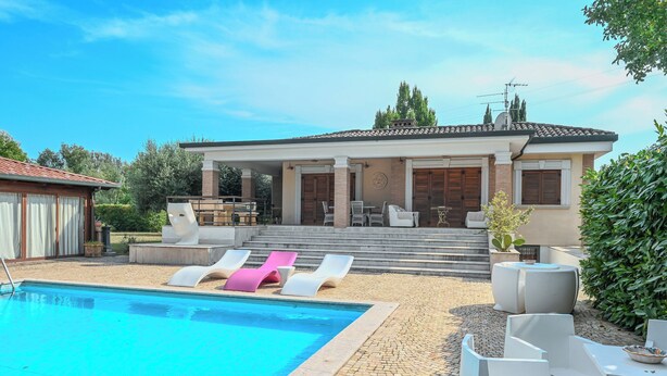 A poolside area with lounge chairs, a covered patio, and a view of a house with a tiled roof and steps leading to the entrance. - Villa Leproso (Benevento)
