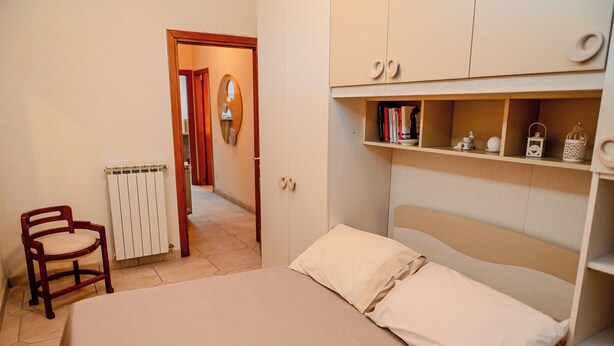 Un dormitorio con cama, una silla, radiador y armario con estantes.