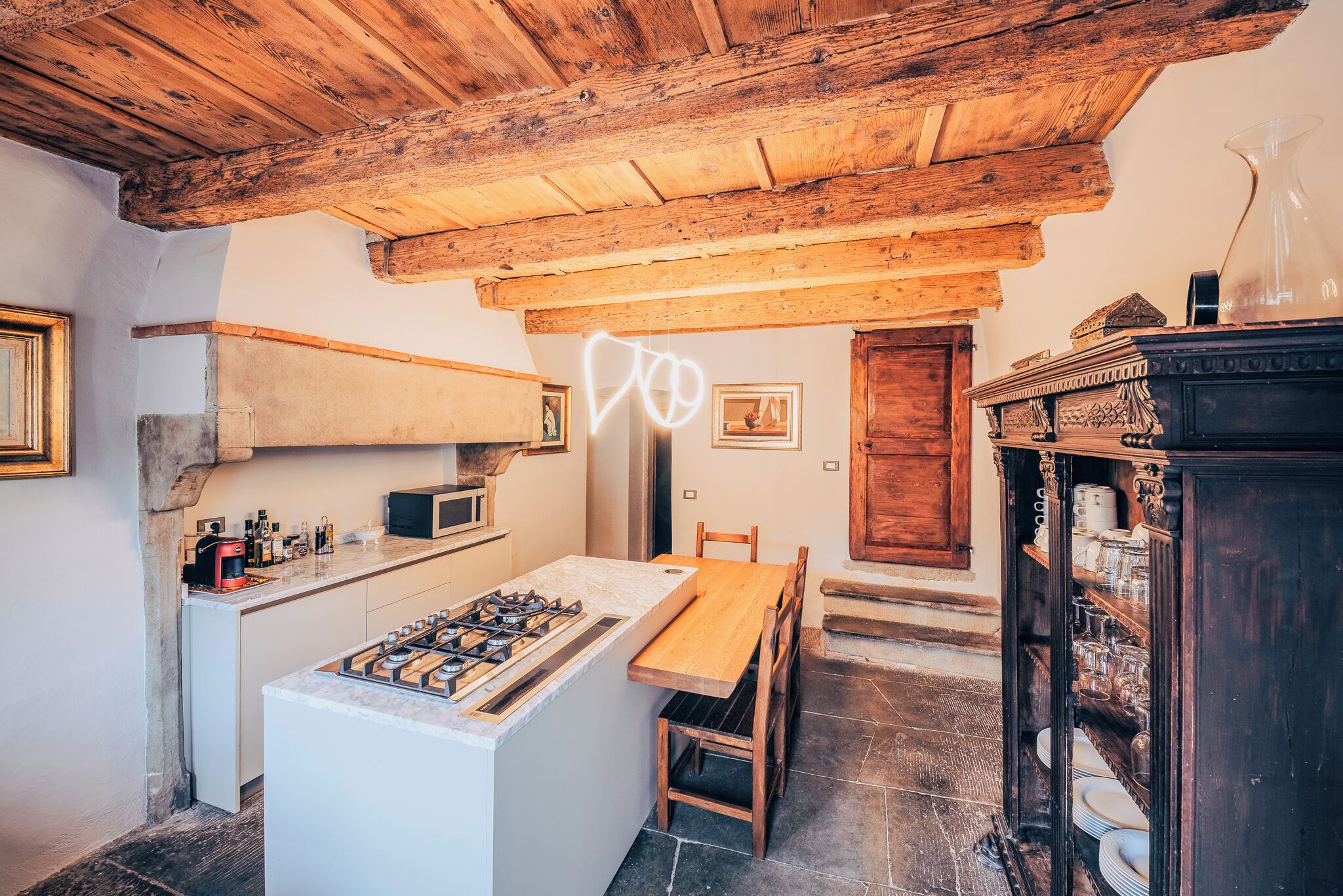A rustic kitchen with a wooden ceiling, a gas stove, a wooden table, and a cabinet with dishes.