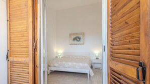 A bedroom with a bed, two bedside tables, a nightstand, and a framed picture on the wall. - Villa Magnolia (Sabaudia)