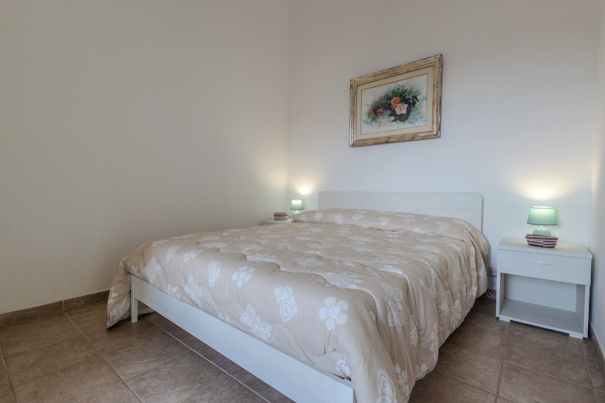 A bedroom with a bed, nightstands, a lamp, and a framed picture on the wall.