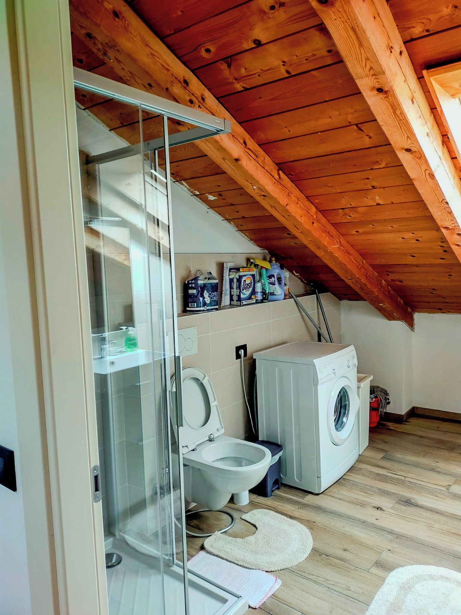 A compact bathroom with a toilet, washing machine, and glass shower enclosure.