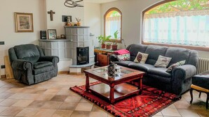 A living room with a fireplace, a sofa, a coffee table, and a window with curtains. - Casa TreSoli - Baselga di Pinè (Baselga di Piné)