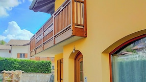 A two-story building with a yellow facade, a wooden balcony, and a window with a curtain. - Casa TreSoli - Baselga di Pinè (Baselga di Piné)
